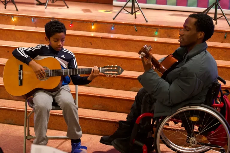 A tutor teaching a boy acoustic guitar on stage